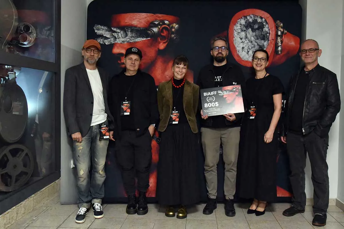 Festival guests holding a prize board in front of the BIAIFF poster
