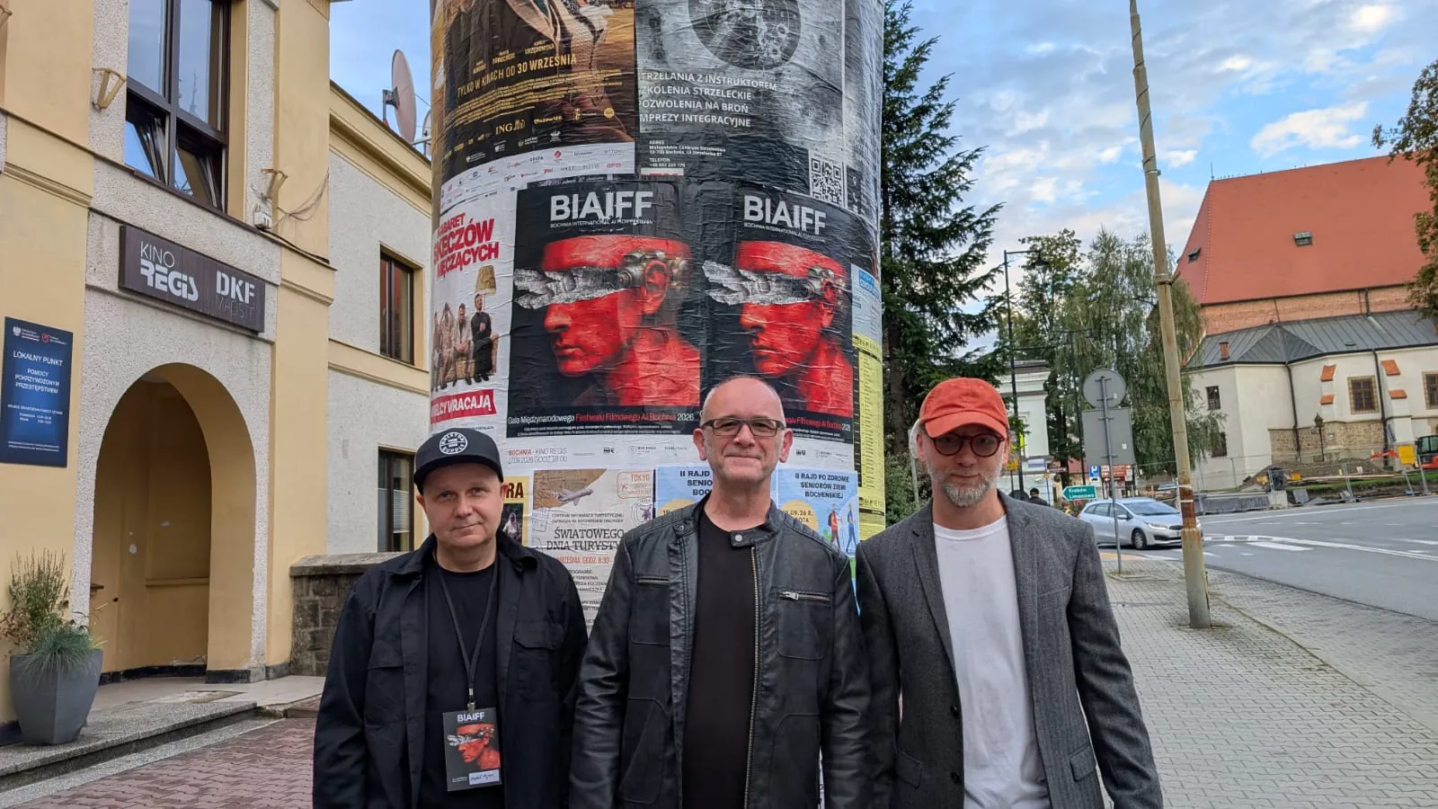 Three festival guests in front of the BIAIFF poster column outside Kino Regis